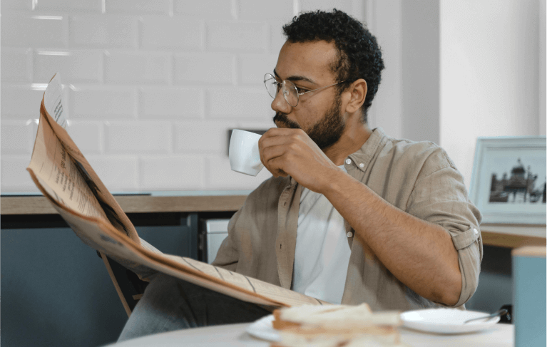 man reading newspaper drinking coffee